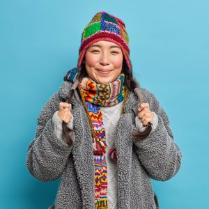 portrait asian woman holds two pigtails smiles pleasantly dressed outerwear knitted hat scarf around neck feels happy isolated blue wall 273609 43770